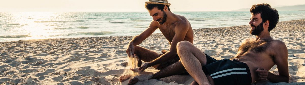 Zwei Männer liegen im Sand und lachen