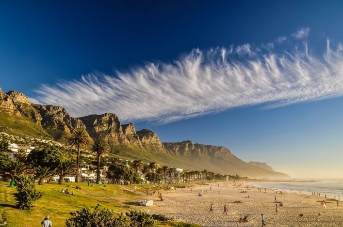 Hohe Felswände, die von der Sonne angestrahlt werden. Im Vordergrund ist Strand.