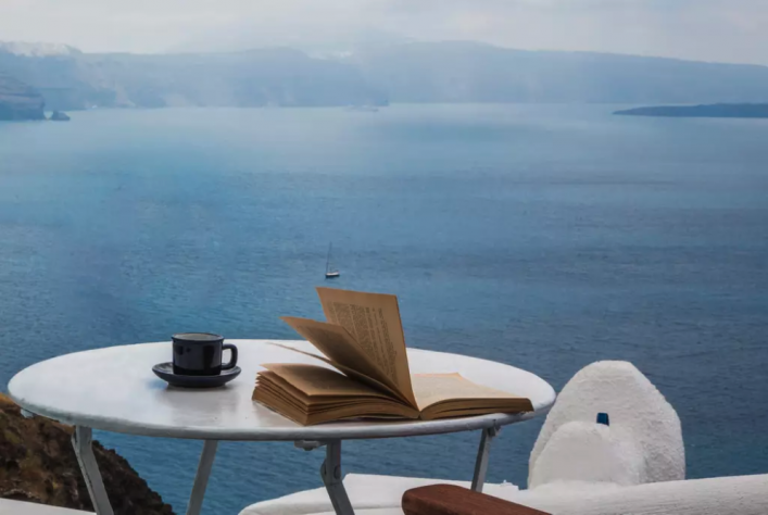Ein Tisch mit einem aufgeschlagenen Buch auf der Terasse der Wohnung, im Hintergrund das Meer.
