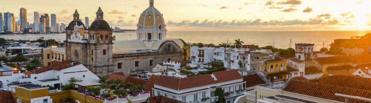 Ein romantischer Sonnenuntergang über dem Meer und den Dächern von Cartagena mit Hochhäusern am Horizont.