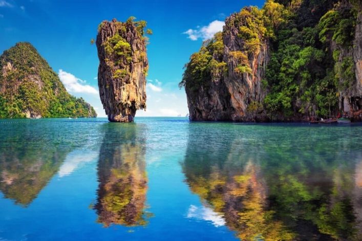 Kalksteinfelsen erheben sich imposant aus dem türkisblauen Wasser. Rechts dichter grüner Dschungel, links ein einzelner Felsen. Die klare Spiegelung verstärkt die tropische Idylle.