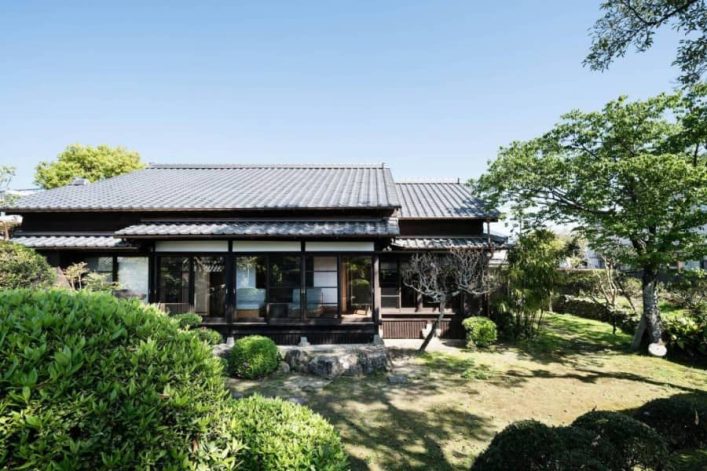 Ferienhaus im traditionell japanischen Stil auf der südlichen Insel Kyushu. Zu sehen sind die großen Fensterfronten, die typische Dachform und ein gepflegter Vorgarten.