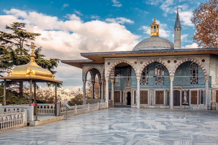 Ein Teil des Topkapi-Palastes in Istanbul mit einer Kuppel und einem schlanken Minarett, umrahmt von Bäumen unter wolkenbedecktem Himmel.