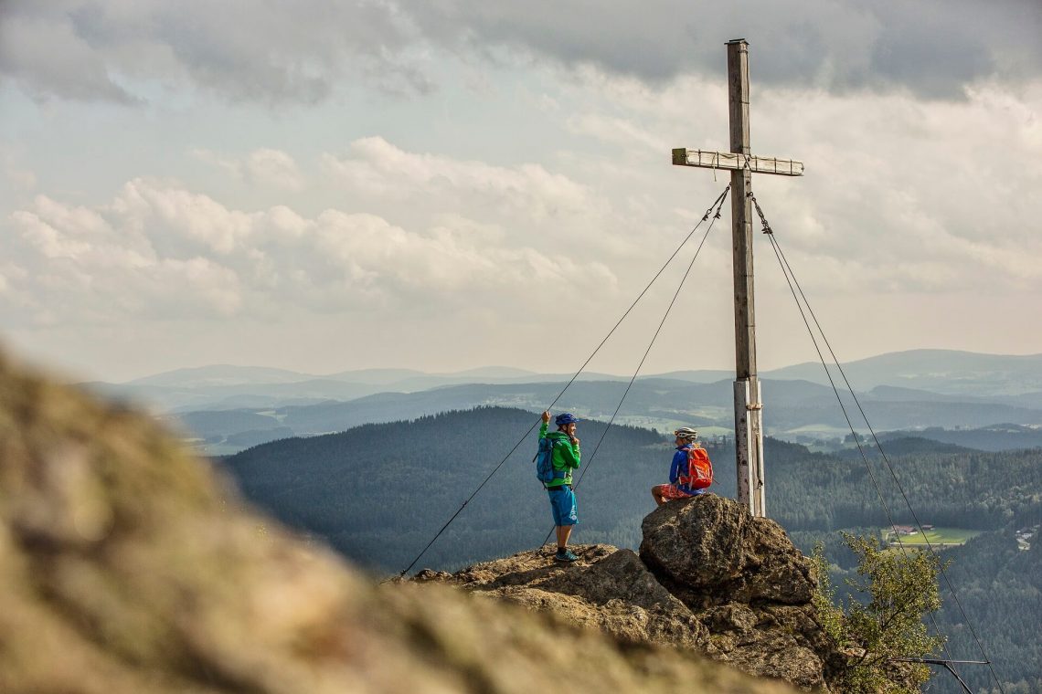 Wanderer am Gipfelkreuz auf dem Großen Arber im Bayerischen Wald.