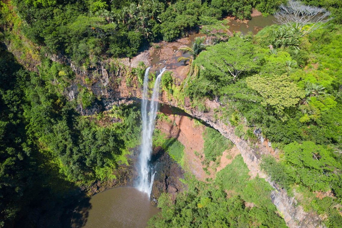 Luftaufnahme eines Wasserfalls, der zentral über eine Felskante in ein Becken fällt, umgeben von üppigem, grünem Wald und Vegetation auf der Insel Mauritius.