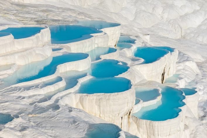 Die Kalksteinterassen von Pamukkale sehen aus, wie eine von Watte übersäte Landschaft, die mittendrin immer wieder Becken hervorbringt, die mit ihrer klaren, hellblauen Farbe ins Auge stechen.