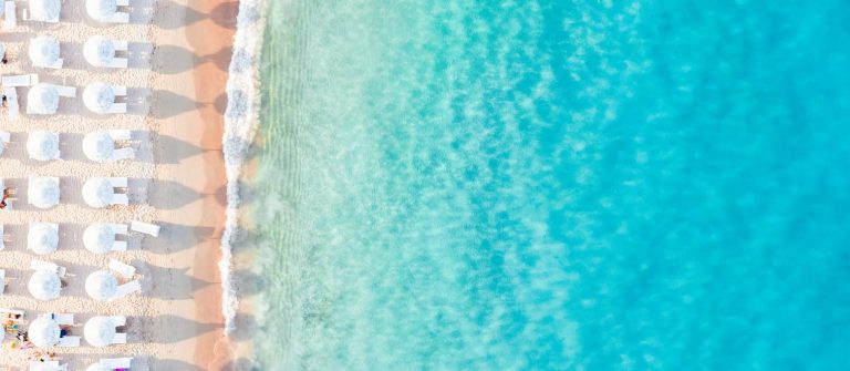 Weiße Sonnenliegen und Sonnenschirme am Sandstrand der Costa Smeralda auf Sardinien