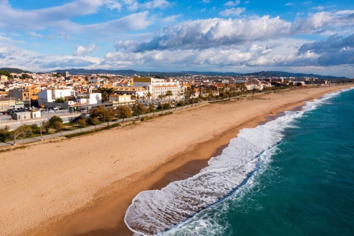 Der goldene Sandstrand von Malgrat de Mar in Katalonien, an der Costa Barcelona. Im Hintergrund beginnt, durch eine Promenade abgetrennt, die Stadt.