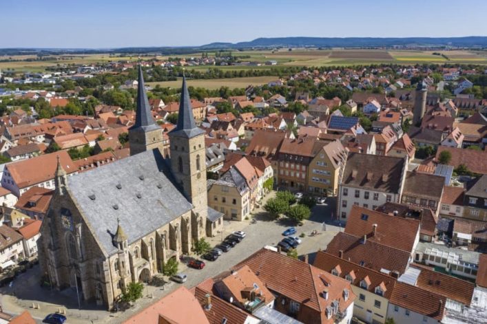 Der Steigerwalddom in Gerolzhofen ist eine Stadtpfarrkirche aus hellem Stein mit Schieferdach und zwei Türmen, umgeben von roten Ziegeldächern der Innenstadt