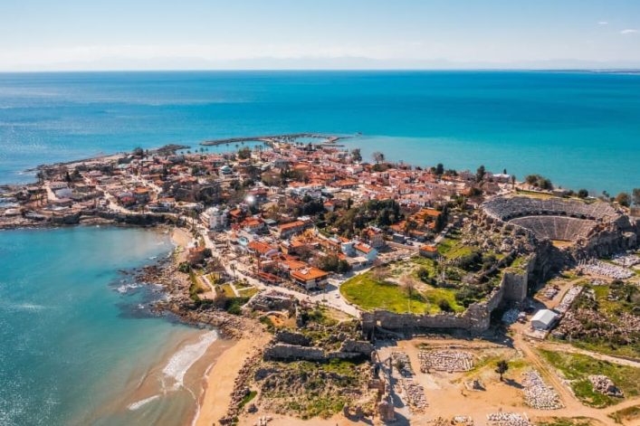 Luftaufnahme der antiken Stadt Side an der türkischen Riviera mit griechischem Theater und Ruinen, umgeben von Meer und modernen Bauten.