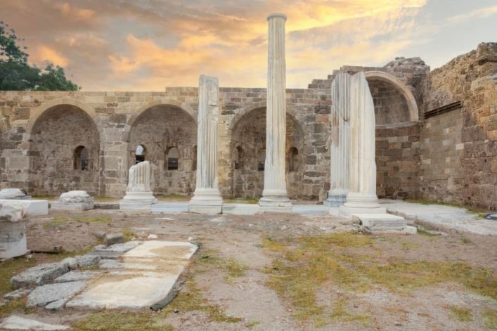 Antike Ruinen des Athena-Tempels in Side: Säulen und Bögen stehen vor einem blassen Himmel, Überreste Geschichte umgeben von Gräsern.
