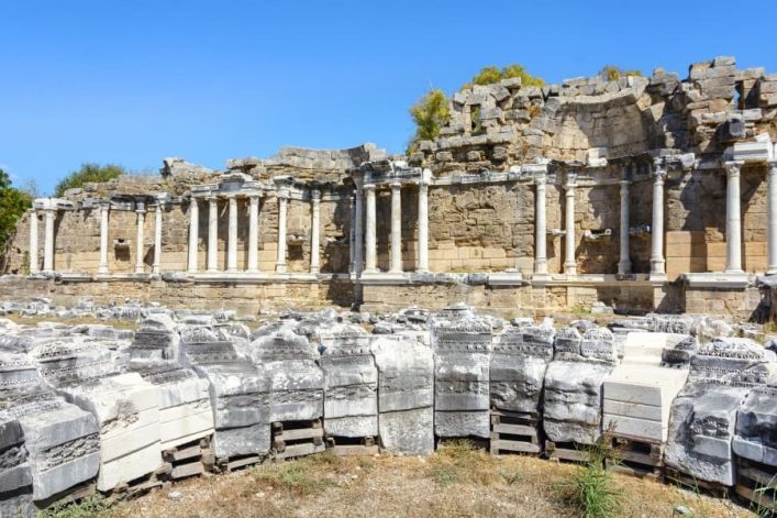 Antike Ruinen des Nymphaeums in Side: Säulen und Bruchstücke im Vordergrund, blauer Himmel im Hintergrund.