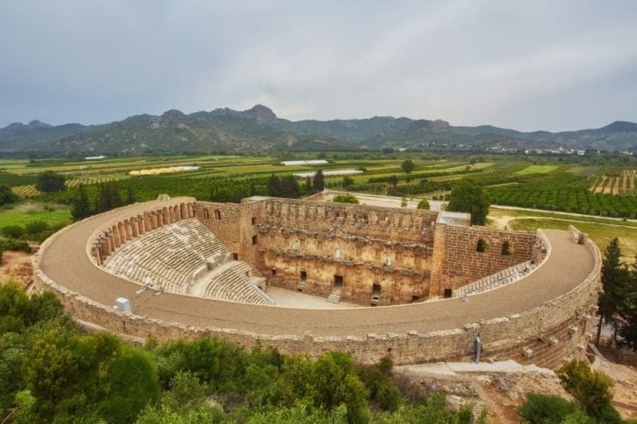 Rundes antikes Theater von Aspendos in der Türkei, umgeben von üppiger Vegetation und Hügeln im Hintergrund.