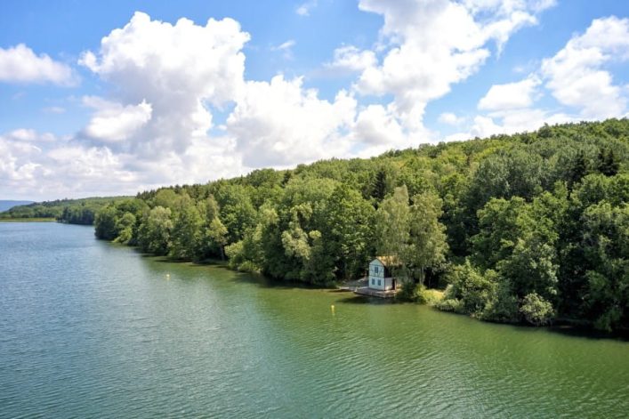Der Ellertshäuser See aus der Luftperspektive. Der See ist groß und blaugrün, an seinem bewaldeten Ufer steht ein kleines Häuschen