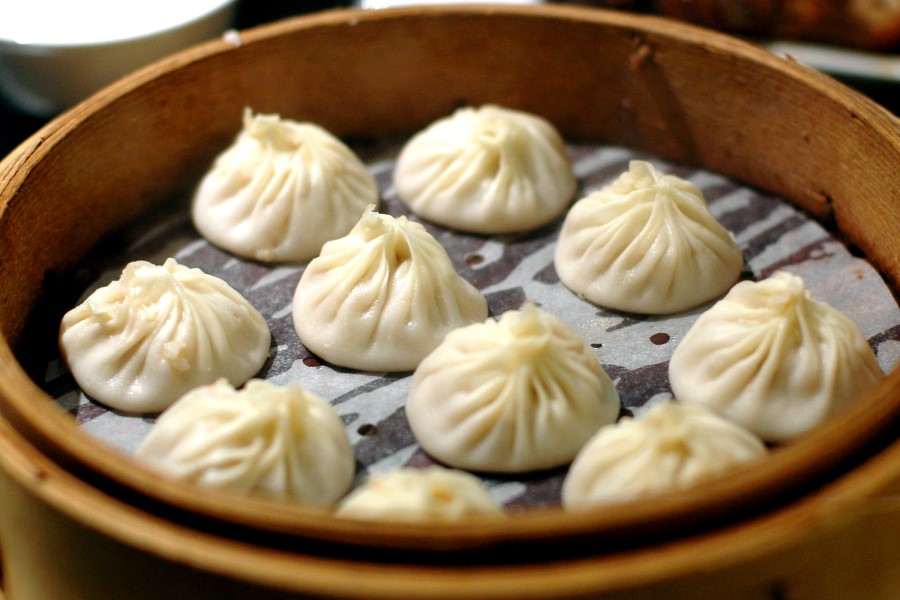 Ein Bambusdämpfer ist mit mehreren runden Teigtaschen gefüllt, die auf Papier liegen und sorgfältig in Reihen angeordnet sind.